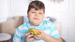 übergewichtiger Junge mit Burger in der Hand