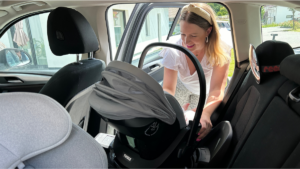 Mama befestigt Babyschale im Auto