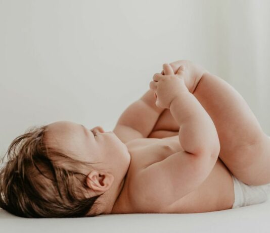 Baby liegt auf dem bett und hält sich an den Füßen.