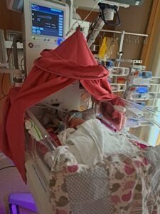 Umgeben von piepsenden Geräten liegt ein Baby auf der Neonatologie.